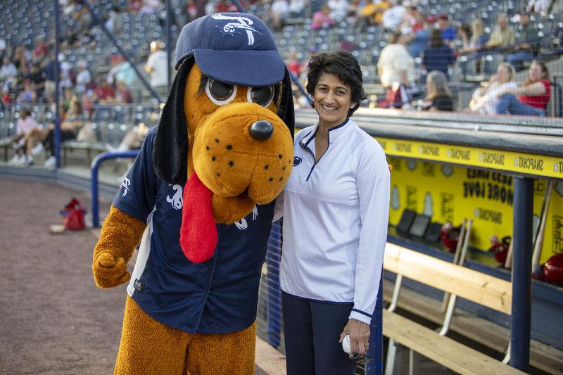 Chancellor Pyati holds a baseball while posing with a hound dog baseball mascot